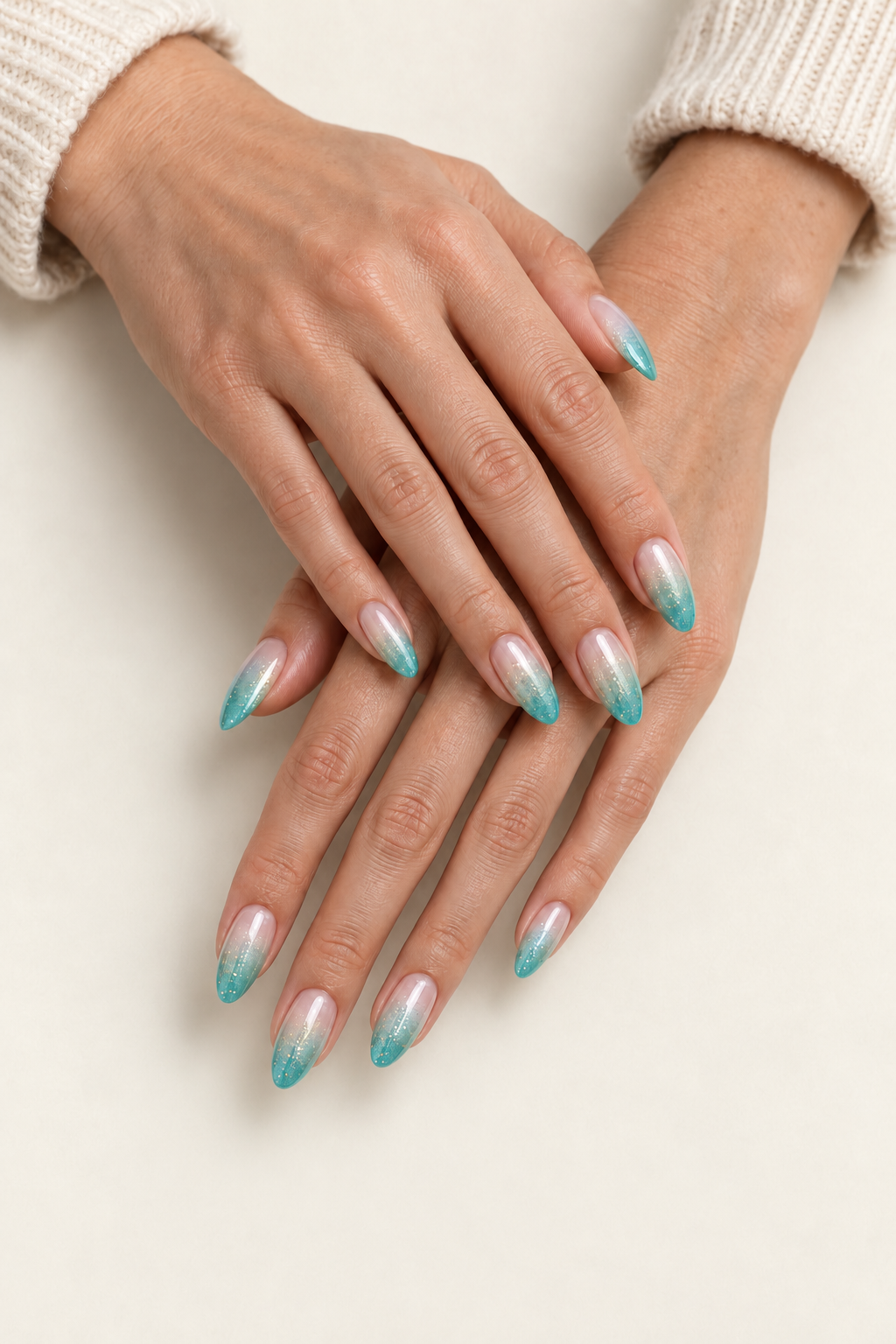 Deux mains croisées aux ongles amande nude et pointes turquoise pailletées