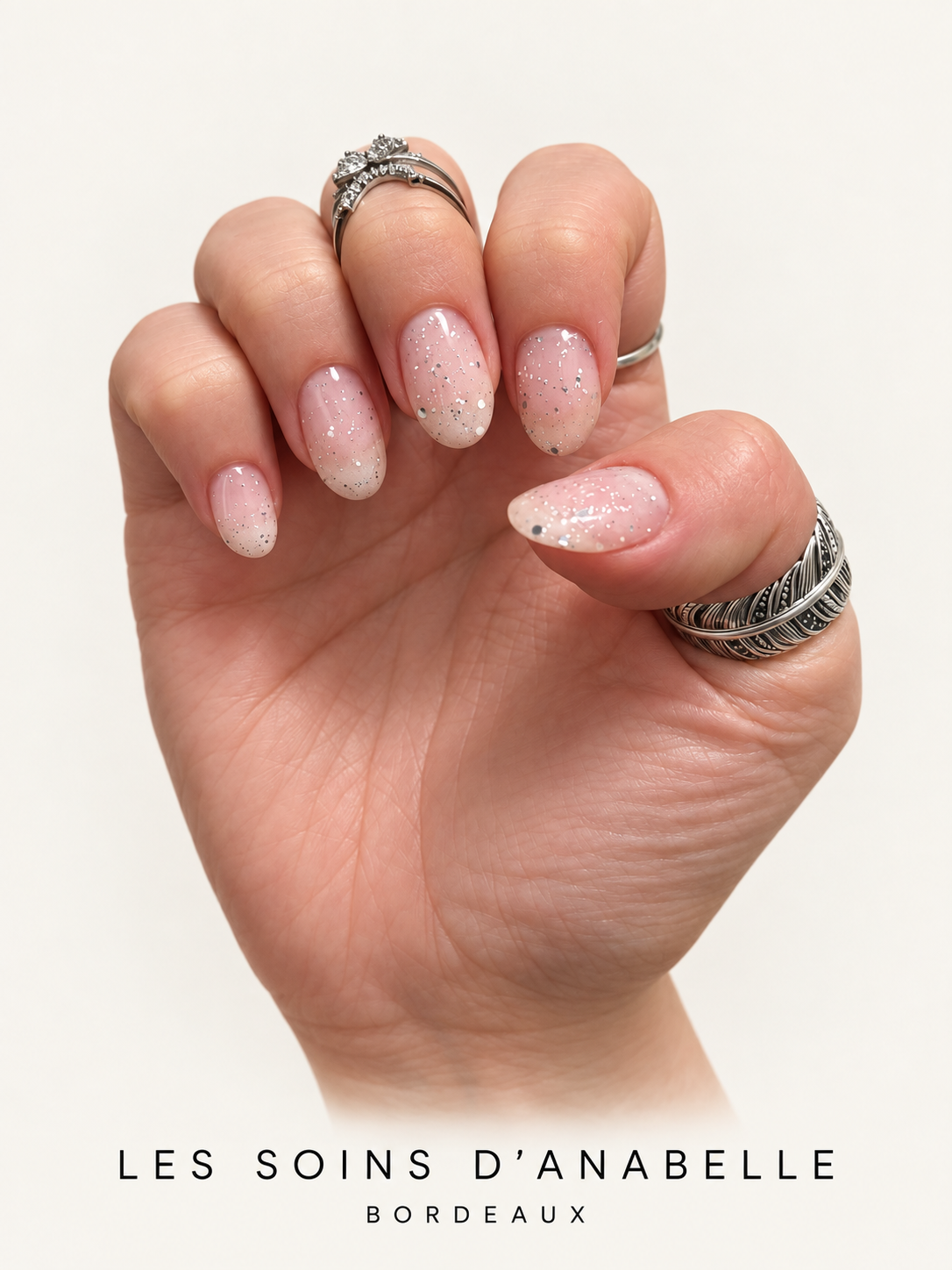 Main aux ongles amande nude pailleté d’argent, pose d’Anabelle en manucure russe